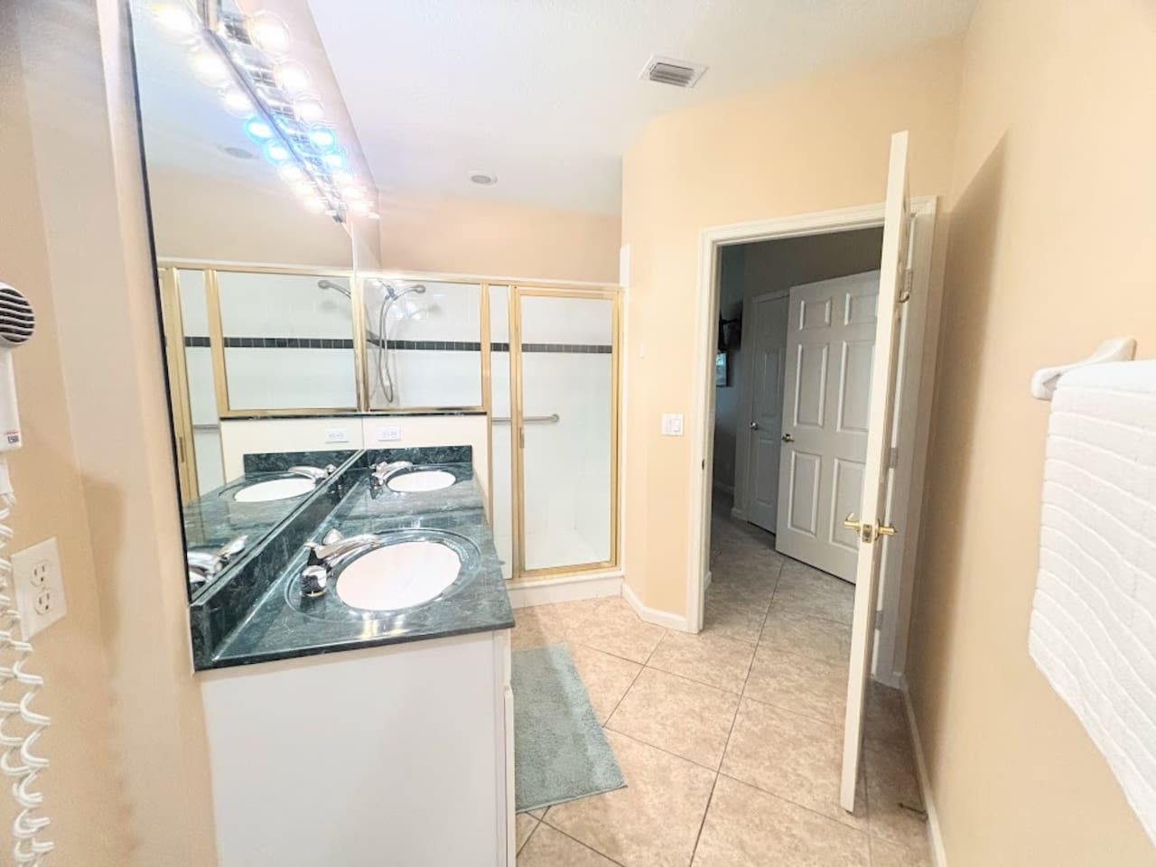 Bright bathroom with large vanity, full mirror, tile flooring, and a walk-in shower with glass doors.