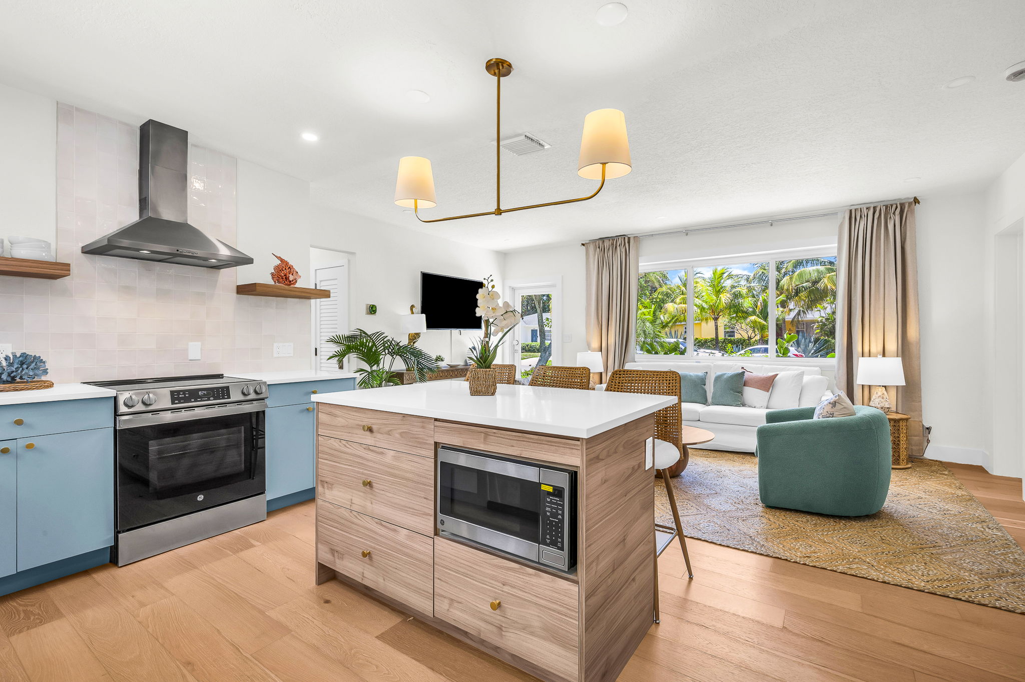 Gourmet kitchen with sleek quartz countertops, custom blue cabinetry, brass accents, and high-end stainless steel appliances. Features an oversized island with seating, open shelving, and designer lighting—perfect for both cooking and entertaining in style
