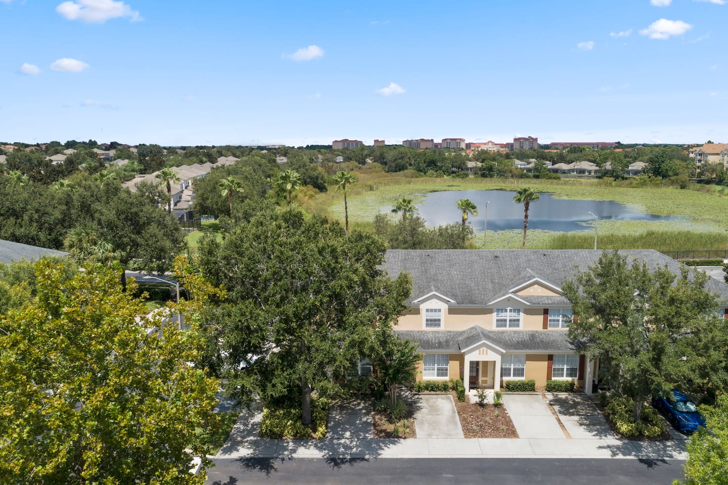 Aerial view of townhouse with nearby pond and trees.

