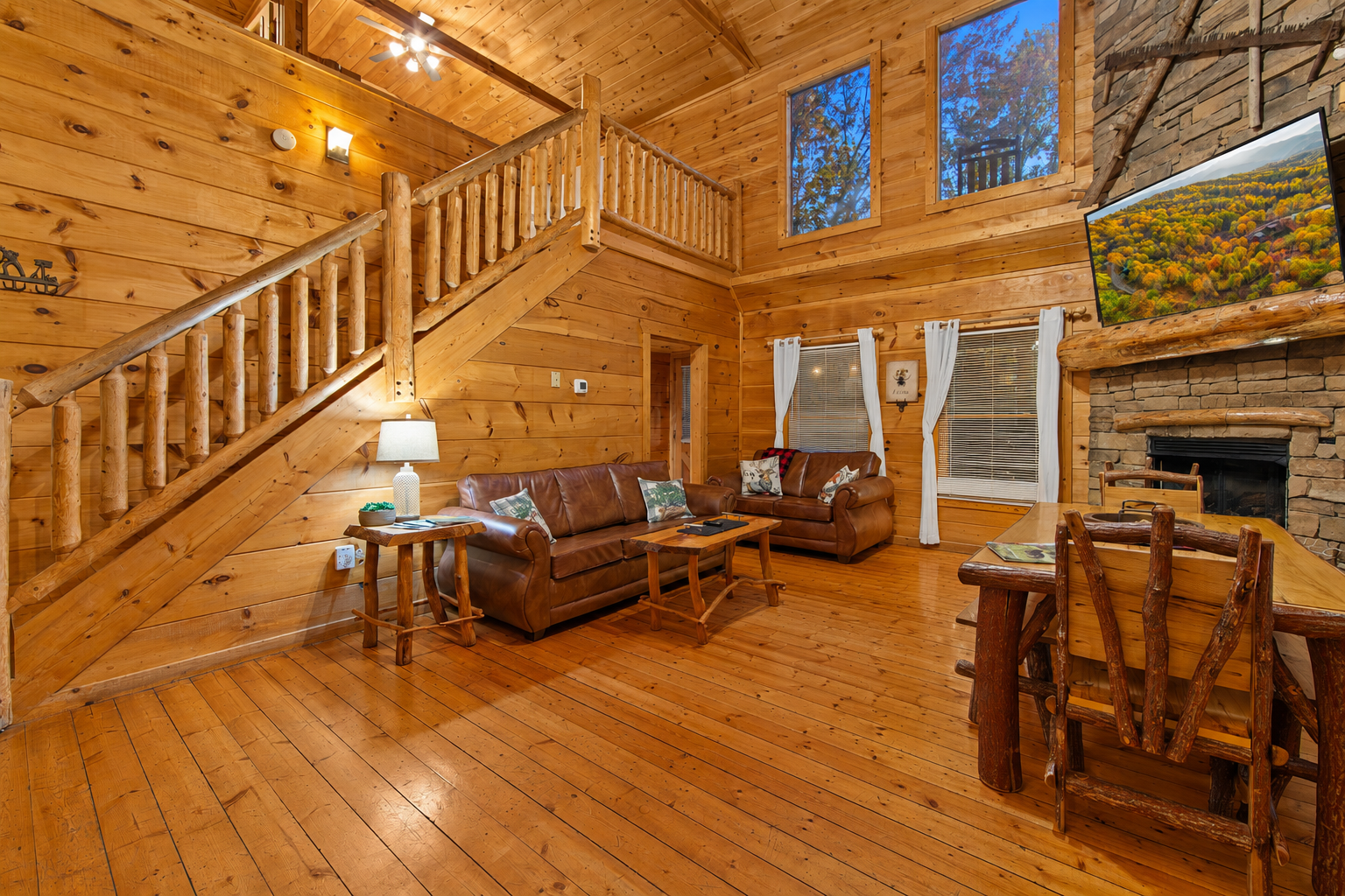 This open-concept cabin living area boasts cozy leather couches, a rustic wooden staircase, and a fully equipped kitchen with black appliances, all set within a warm, wood-paneled interior.