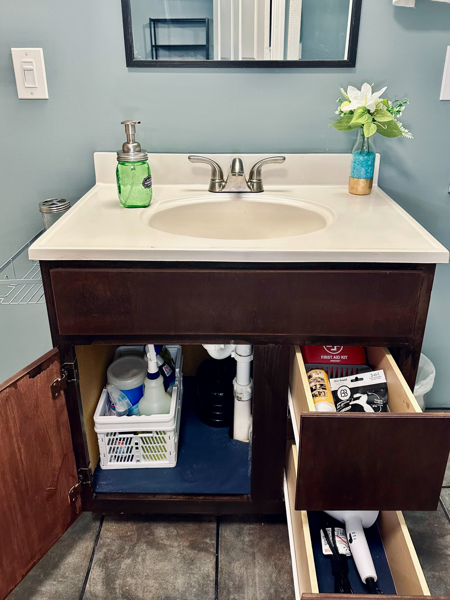Basement bathroom cabinet stocked with bathroom-specific cleaning products and drawers including a lint roller, first aid kit, hair dryer, and toothbrushes/toothpaste (stored inside). Stocked so guests using the lower level have everything they need.