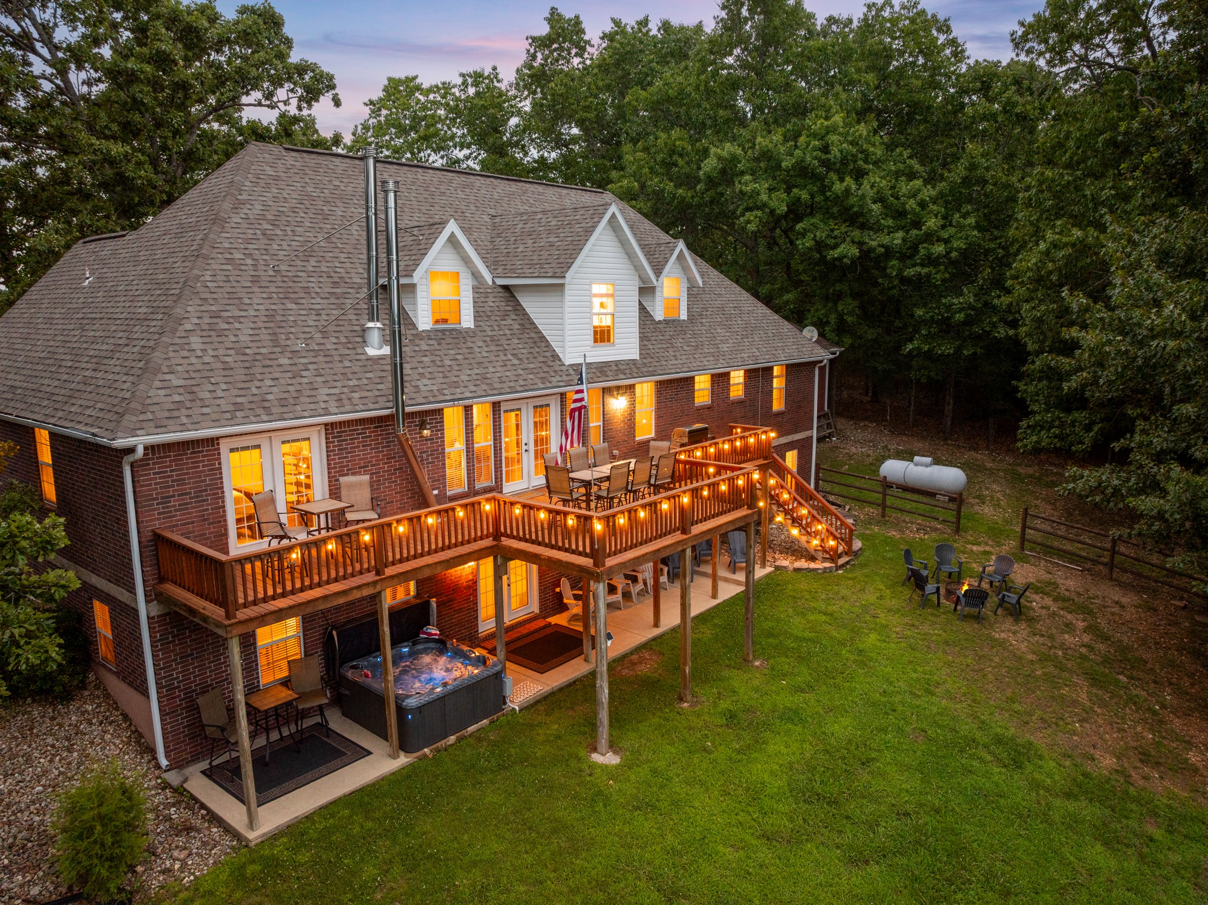 Dusk view of the back deck, hot tub and fire pit. The private hot tub sits below the lit deck, with the fire pit out on the lawn.