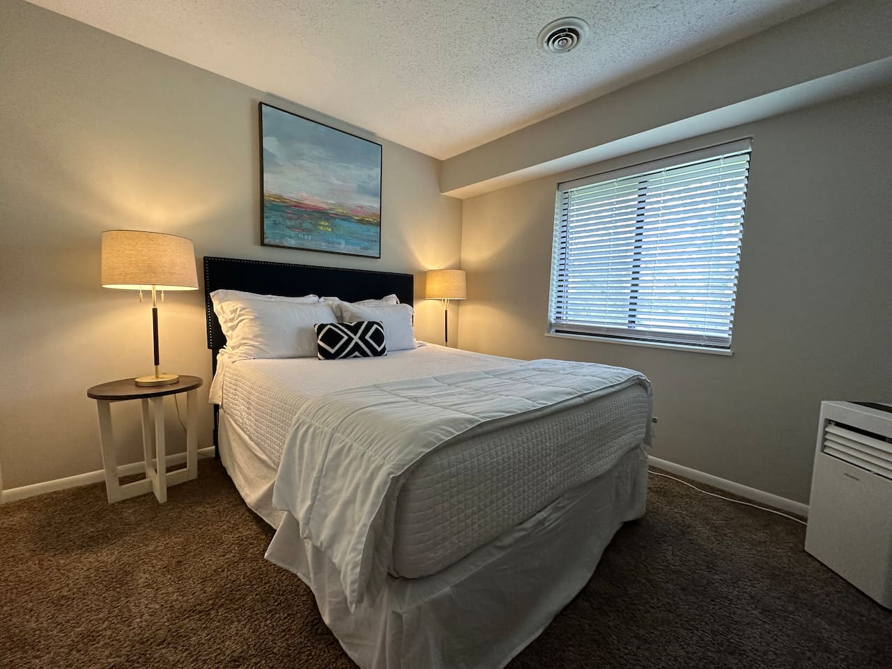 Relax in a cozy queen bed with plush bedding, soft lighting, and peaceful natural light.