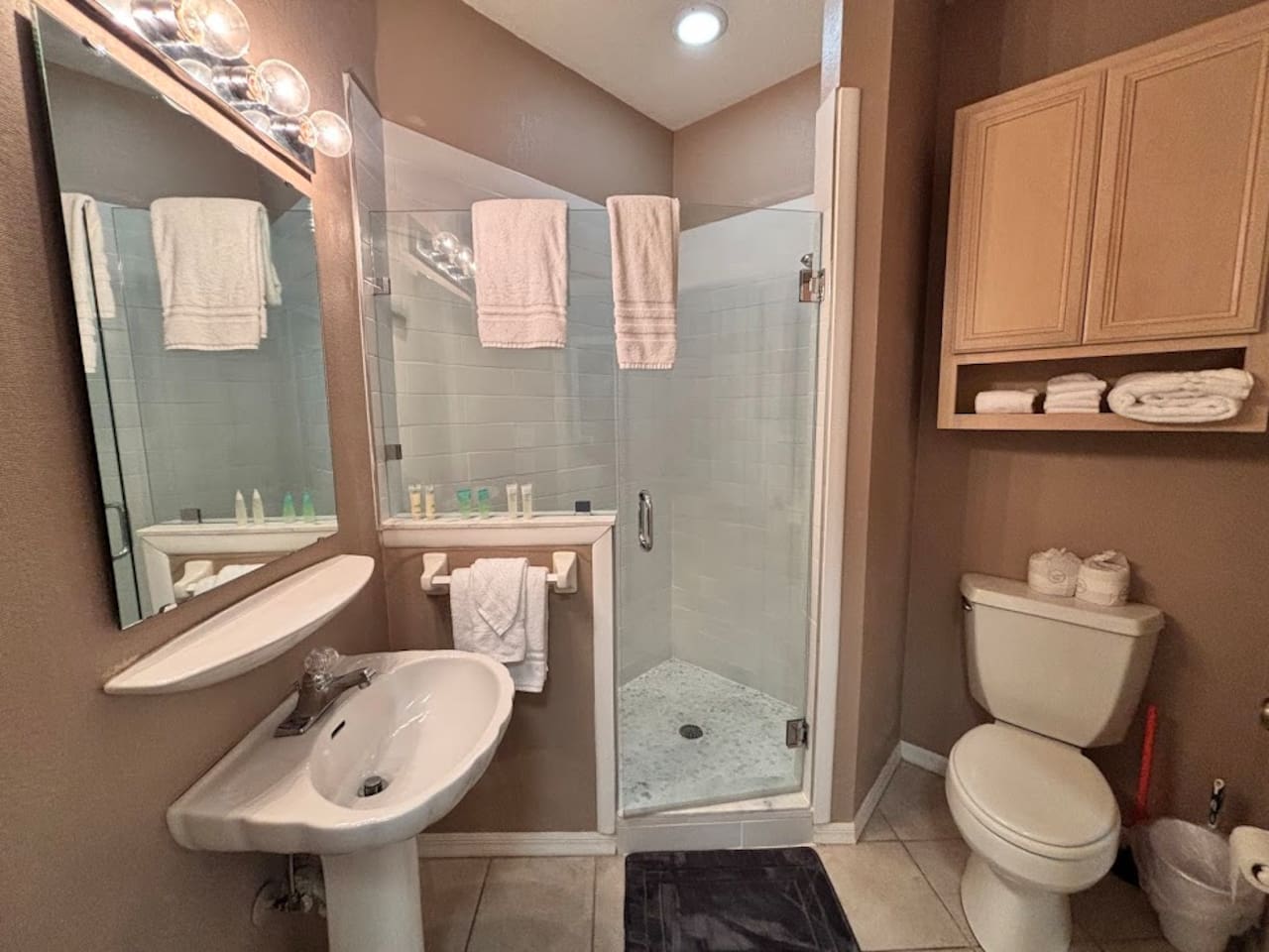 Bathroom featuring a pedestal sink, bright vanity lighting, glass-enclosed shower, and clean neutral finishes.