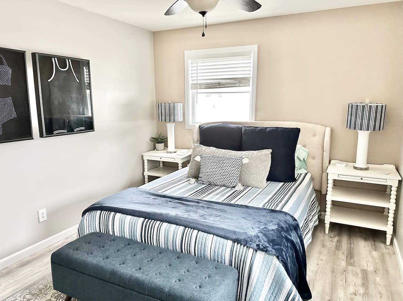 Relax in this beautifully appointed guest room, featuring a tufted headboard and a plush bed layered with navy and white striped linens. Two matching bedside tables with striped lamps and a comfortable storage bench complete this tranquil coastal escape.