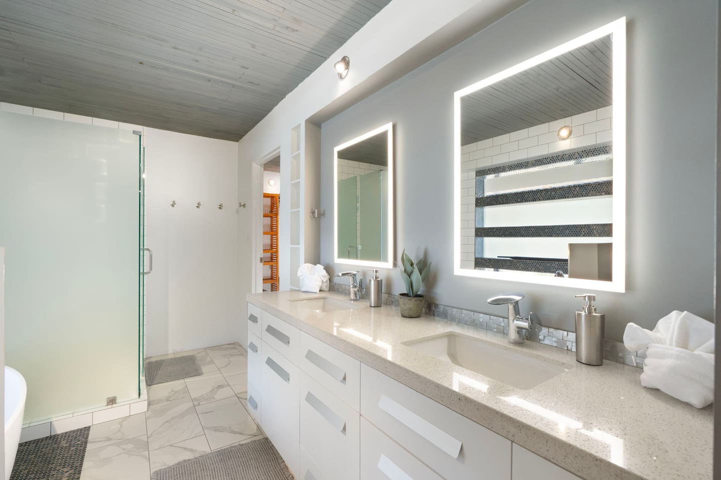 Bright and modern bathroom with a double vanity, illuminated mirrors, and a spacious walk-in glass shower — thoughtfully designed for comfort and convenience.