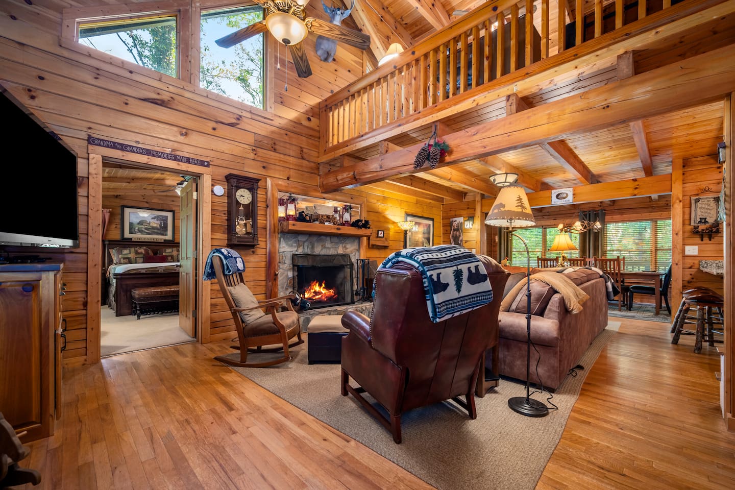 Warm and inviting great room featuring soaring, vaulted ceilings, floor-to-ceiling wood interiors, a cozy stone fireplace, and comfortable seating. The open-concept layout creates the perfect gathering place for family and friends.