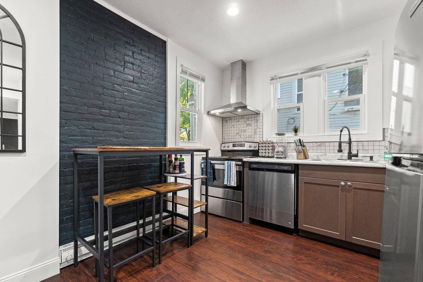 Modern and cozy kitchen featuring stainless steel appliances, a stylish black accent wall, and a charming dining nook. Fully equipped for all your cooking needs!