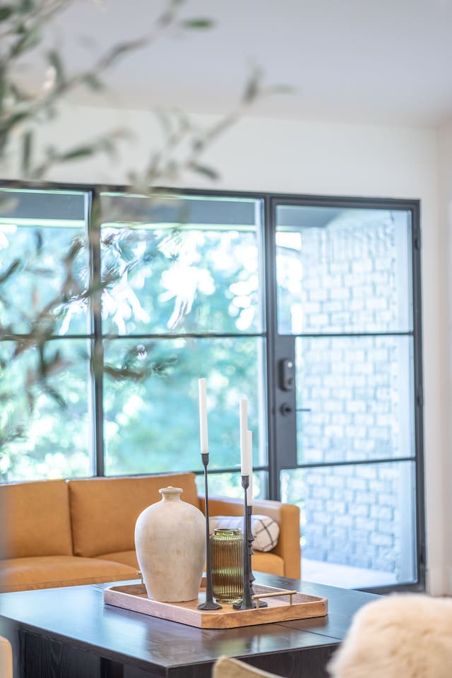 Living room detail featuring a styled coffee table with curated décor, warm wood tones, and natural light from oversized windows.