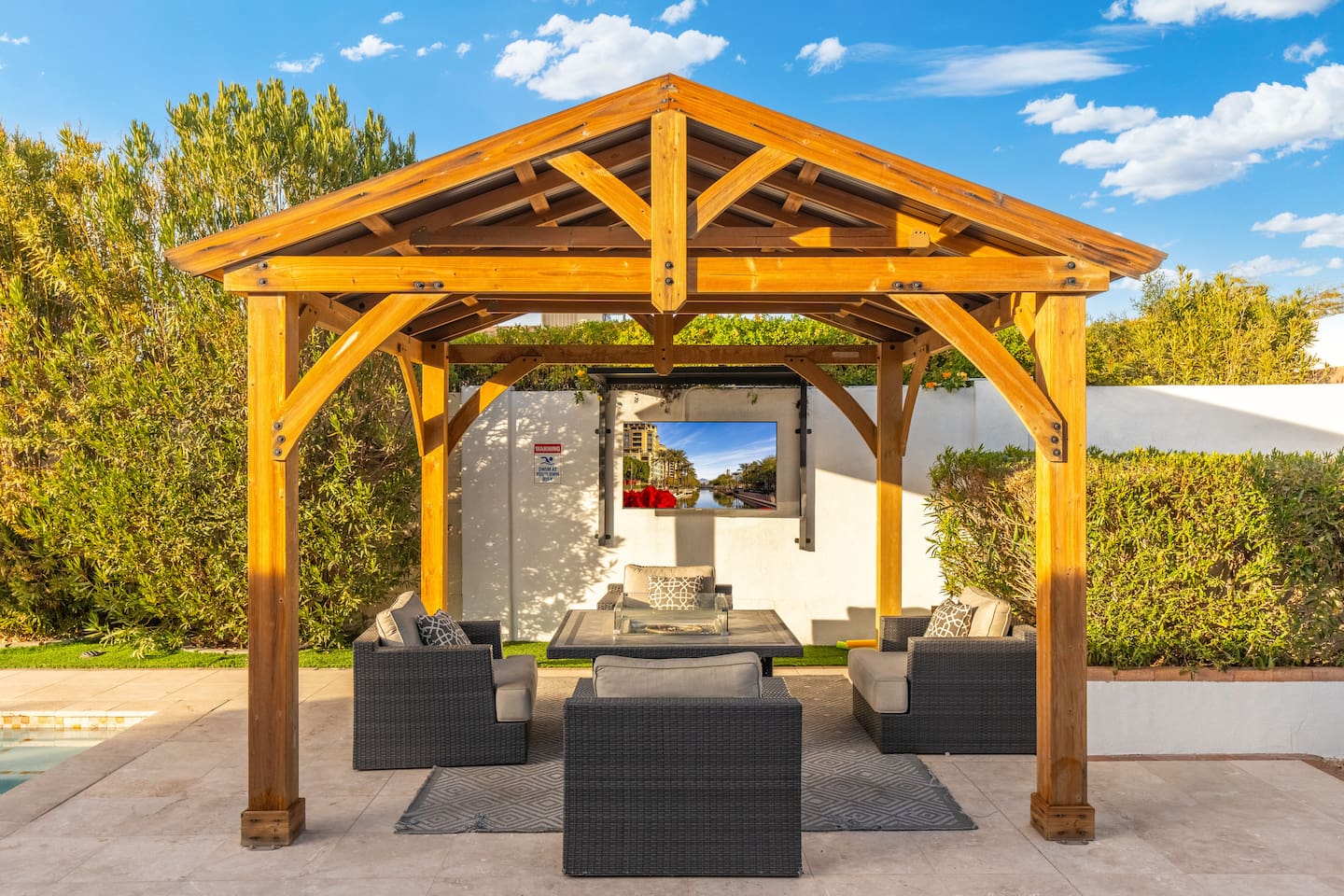 Enjoy the perfect blend of comfort and entertainment beneath the wooden pergola, complete with a cozy fire table and an outdoor TV.