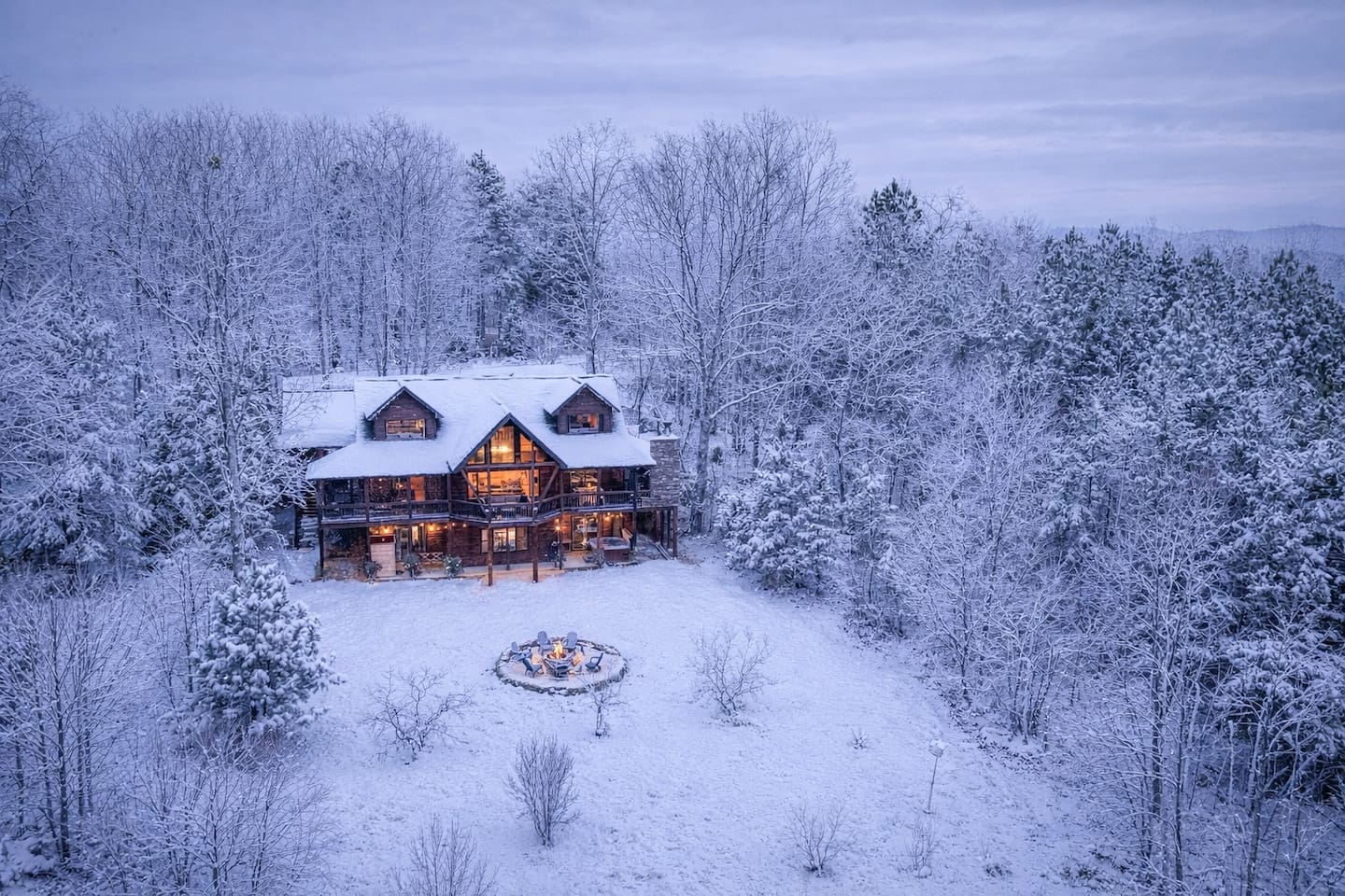 SNOW! The back of the beautiful "Blessed Sunset" mountain retreat home overlooking the back yard! Stunning A-frame, wrap-around porch, screened-in patio, outdoor fireplace, outdoor dining table, sauna, hot tub, outdoor couch, and more!