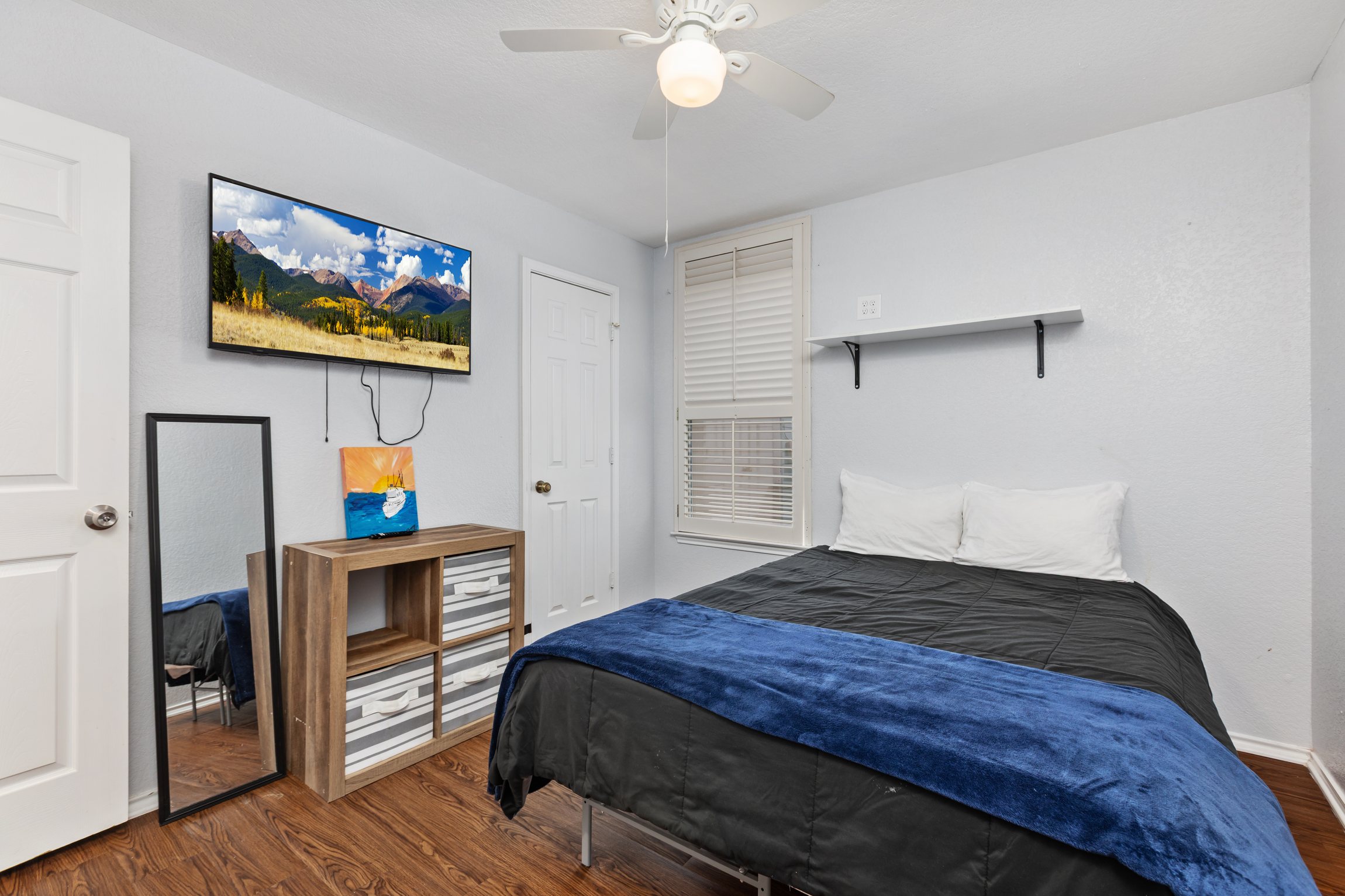 Bedroom with wall-mounted Smart TV, streaming access, dresser for clothing storage, ceiling fan, and hotel-quality bedding. Extra pillows and blankets included. Current decorative blankets, bedding, and wall art are not shown in these photos.