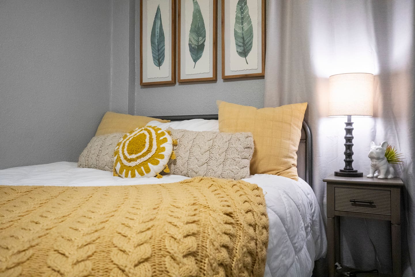Close-up of a cozy queen bed adorned with cute throw pillows, complemented by a stylish side table and lamp for added comfort and ambiance.