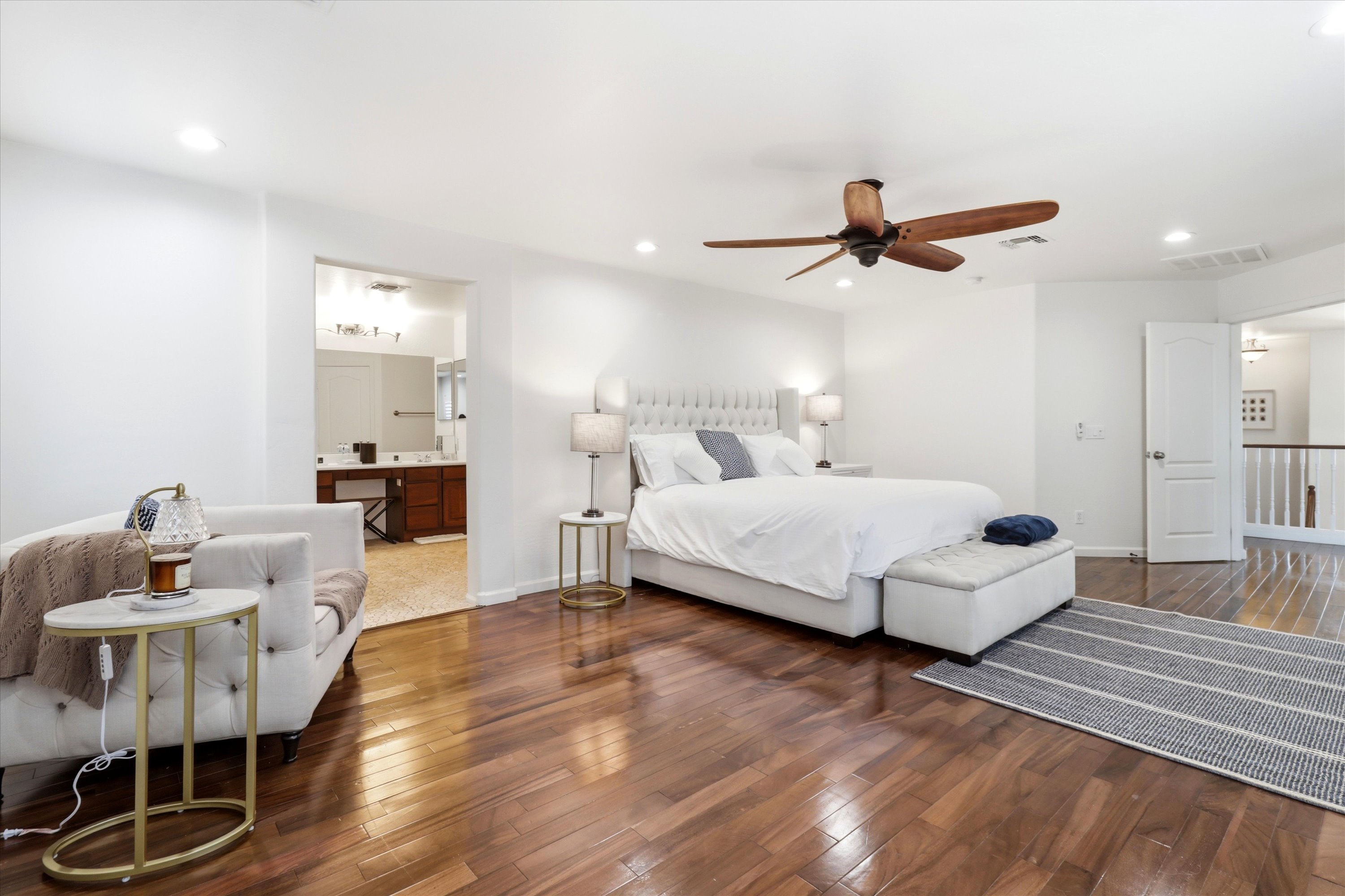 Primary bedroom with a large bed, sitting chair, wood floors, and easy access to the ensuite bathroom.
