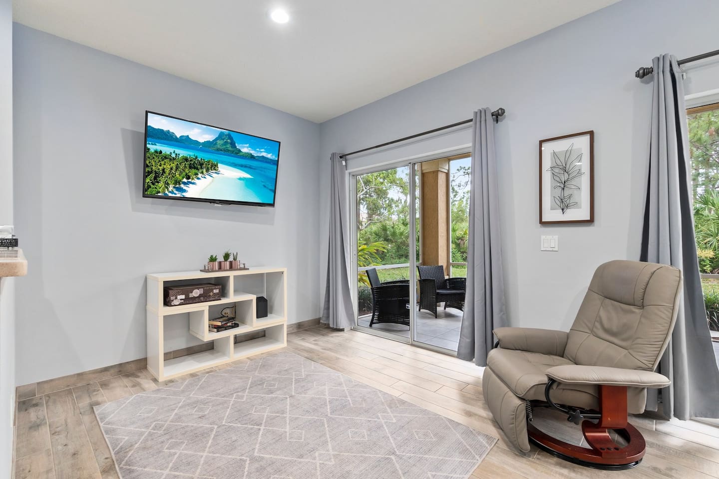 Bright living area featuring a wall-mounted TV, comfortable recliner, and direct access to the screened patio.