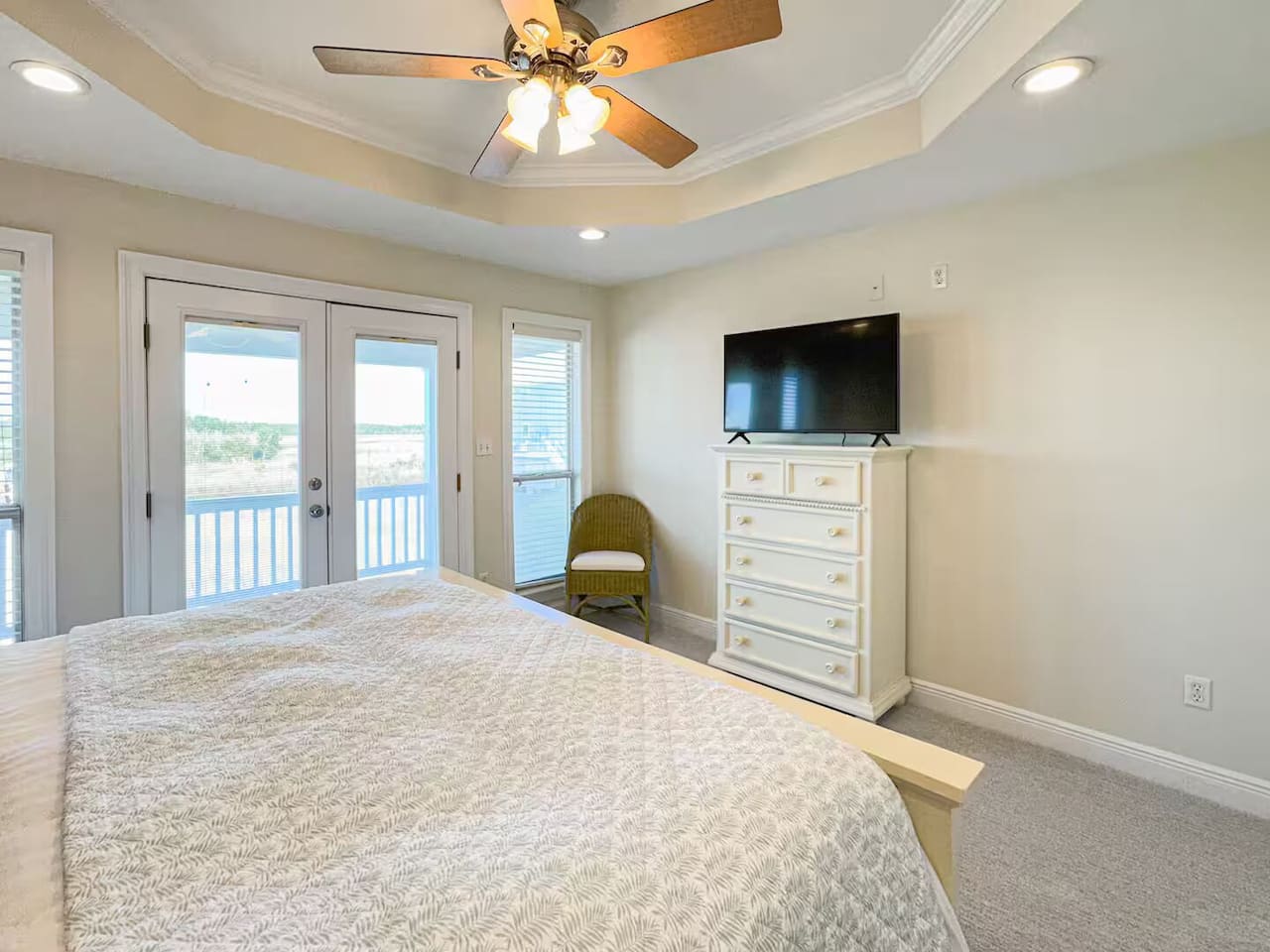 Airy bedroom with a comfortable bed, flat-screen TV, and private balcony access. Features abundant natural light, ceiling fan, and a calm, coastal feel.