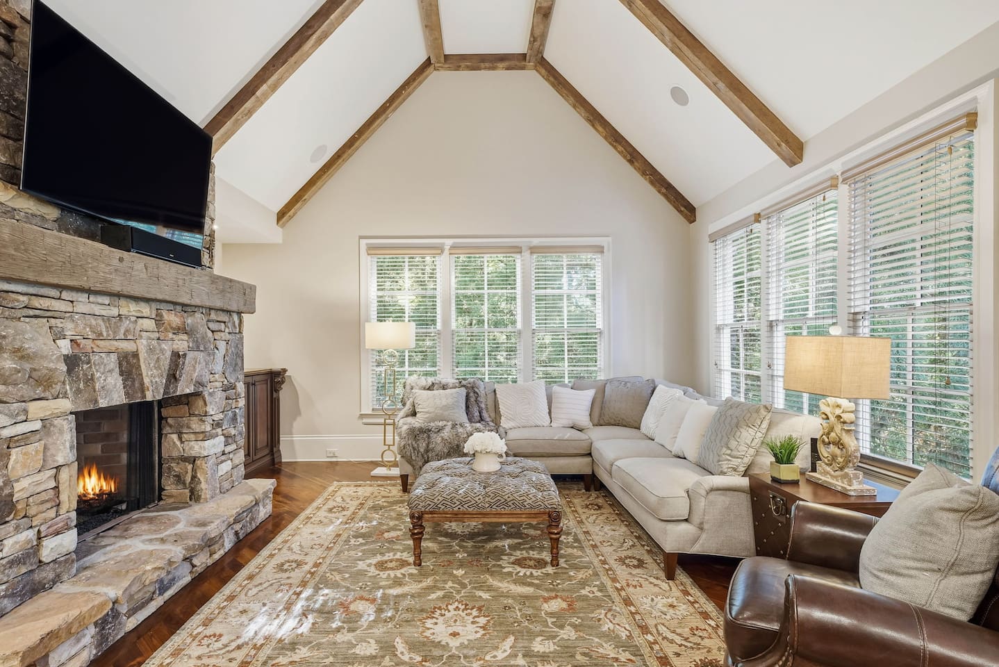 Relax in a warm and welcoming living room featuring high ceilings, a beautiful stone fireplace, and rich wood accents that create a cozy, home-like atmosphere. Enjoy a smart TV with a quality sound system perfect for movie nights and quiet mornings.