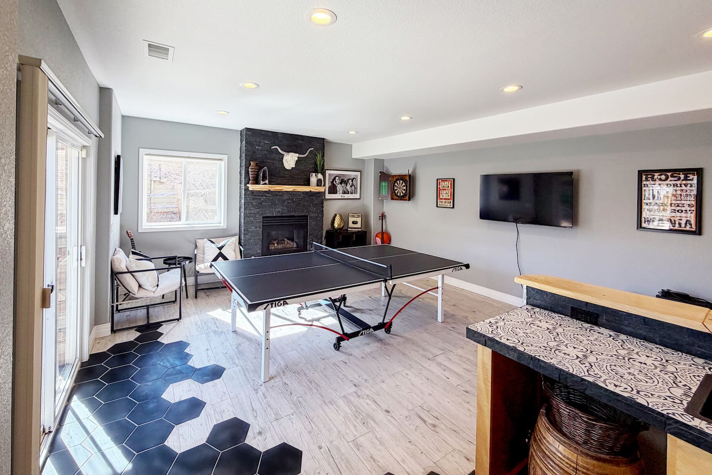 This bright and inviting game room features a sleek ping pong table at the center, perfect for friendly competition and family fun. A cozy stone fireplace, Flat-screen TV and dartboard create the ultimate entertainment space.