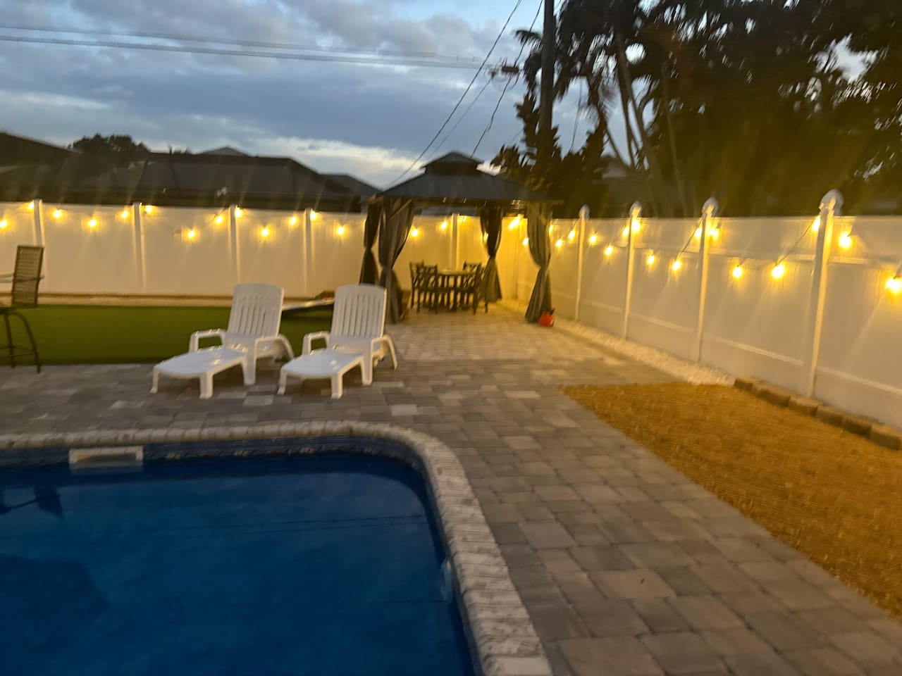 Pool area in the evening when the lights are on gazebo and launge chairs 