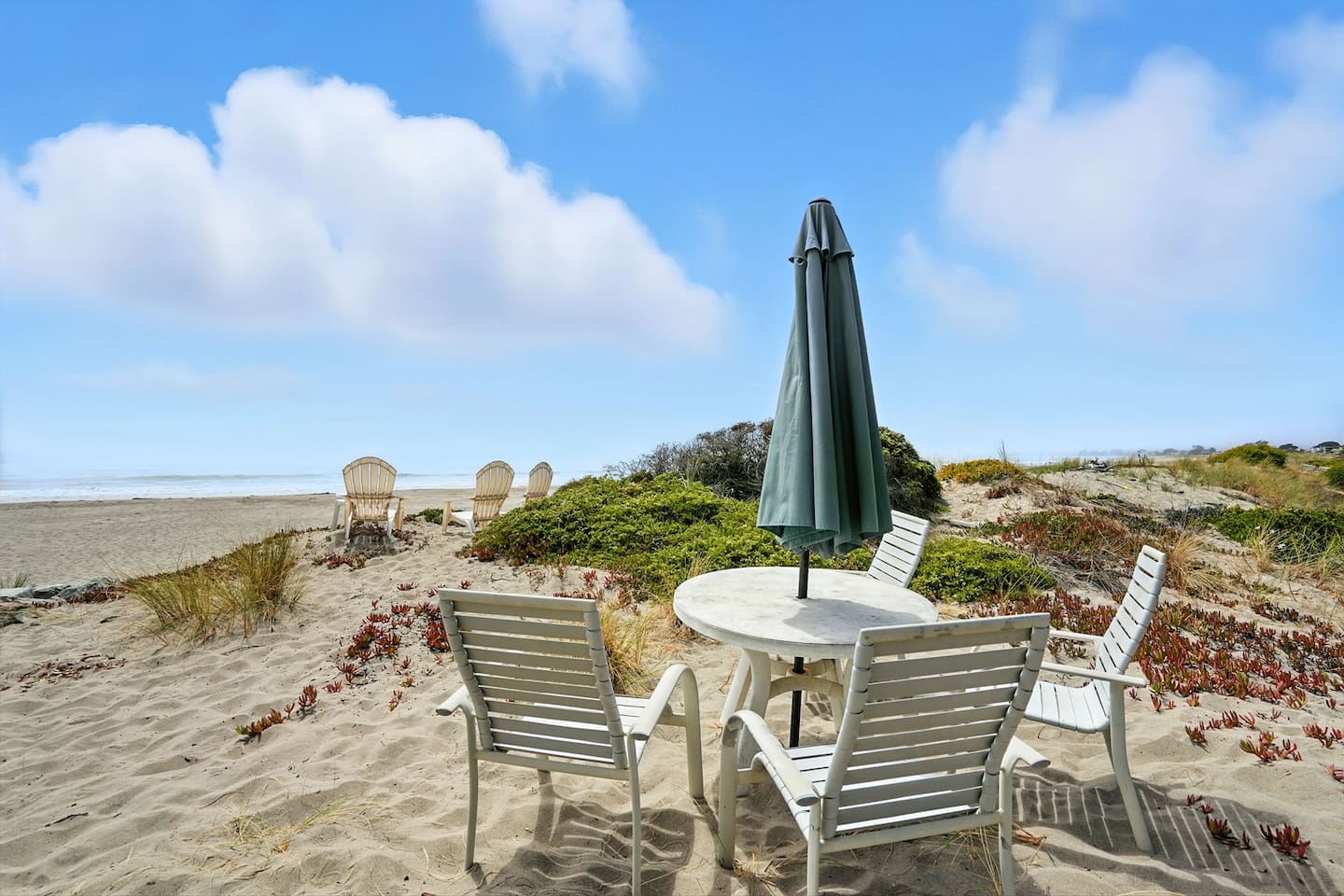 Outdoor dining set on sandy beach with umbrella shade.

