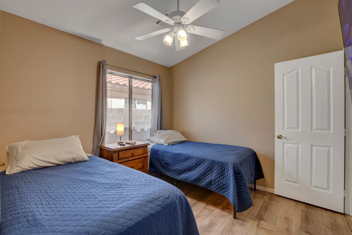 Cozy twin bedroom with natural light, ceiling fan, and wood floors