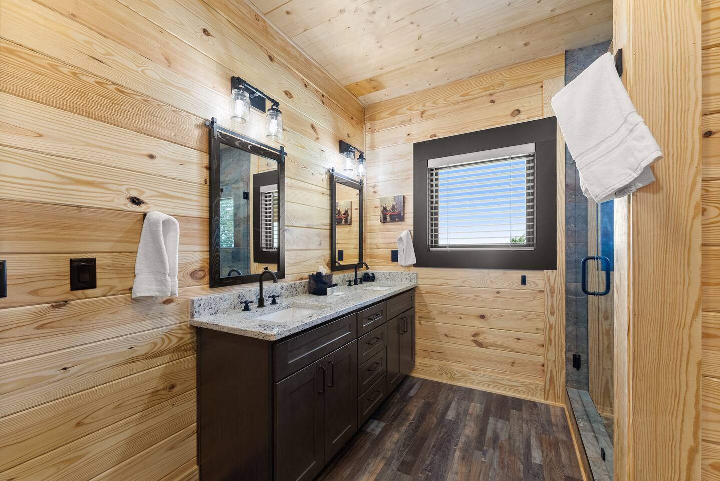 Elegant dual-sink vanity with granite countertops, matte black fixtures, and rustic wood walls—ideal for shared use with ample storage space.