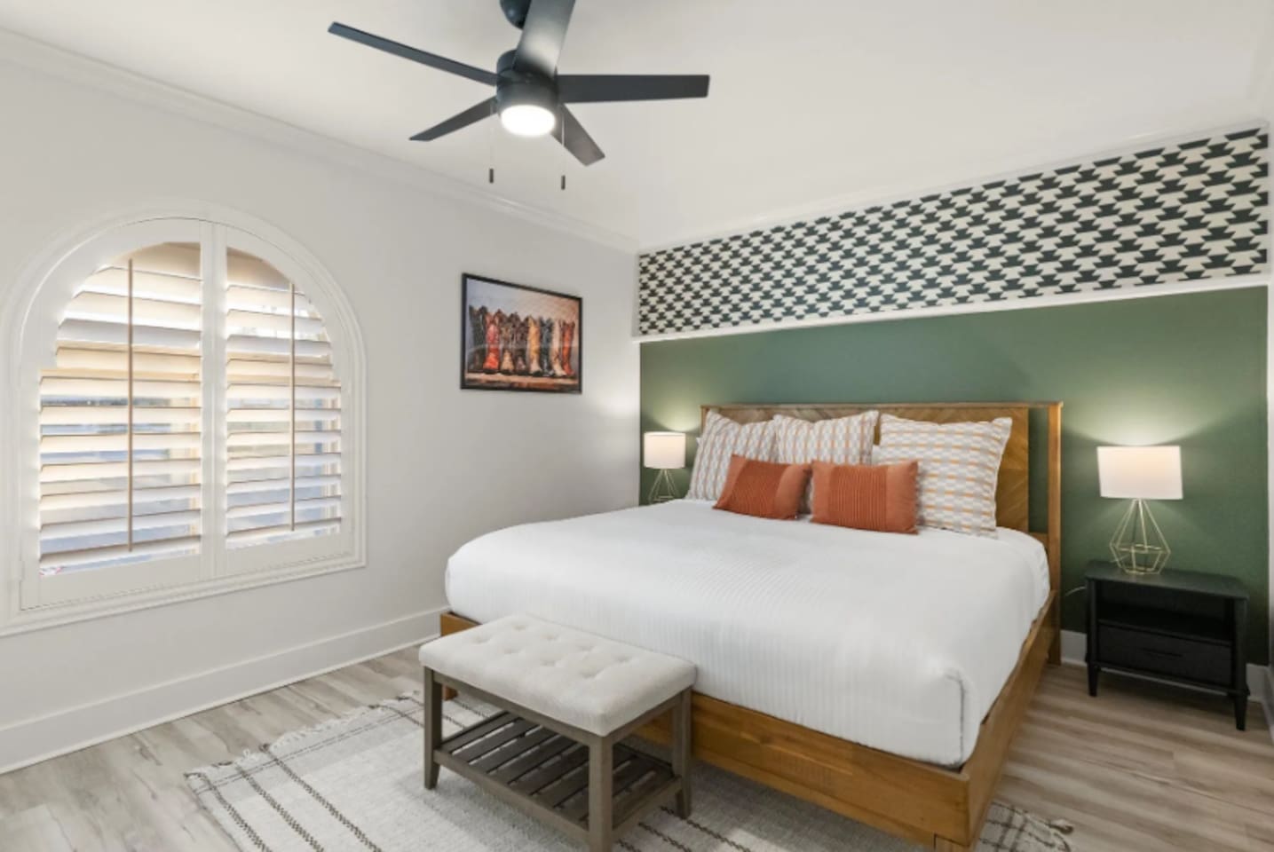 A houndstooth accent and rich green wall frame the king bed, with a playful boot print nodding to the western spirit throughout the home. Arched shutter windows and warm bedside lighting round out a room that feels both cozy and stylish.
