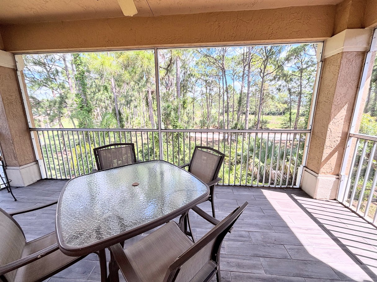 Spacious screened balcony with seating, ceiling fan, and relaxing wooded views.