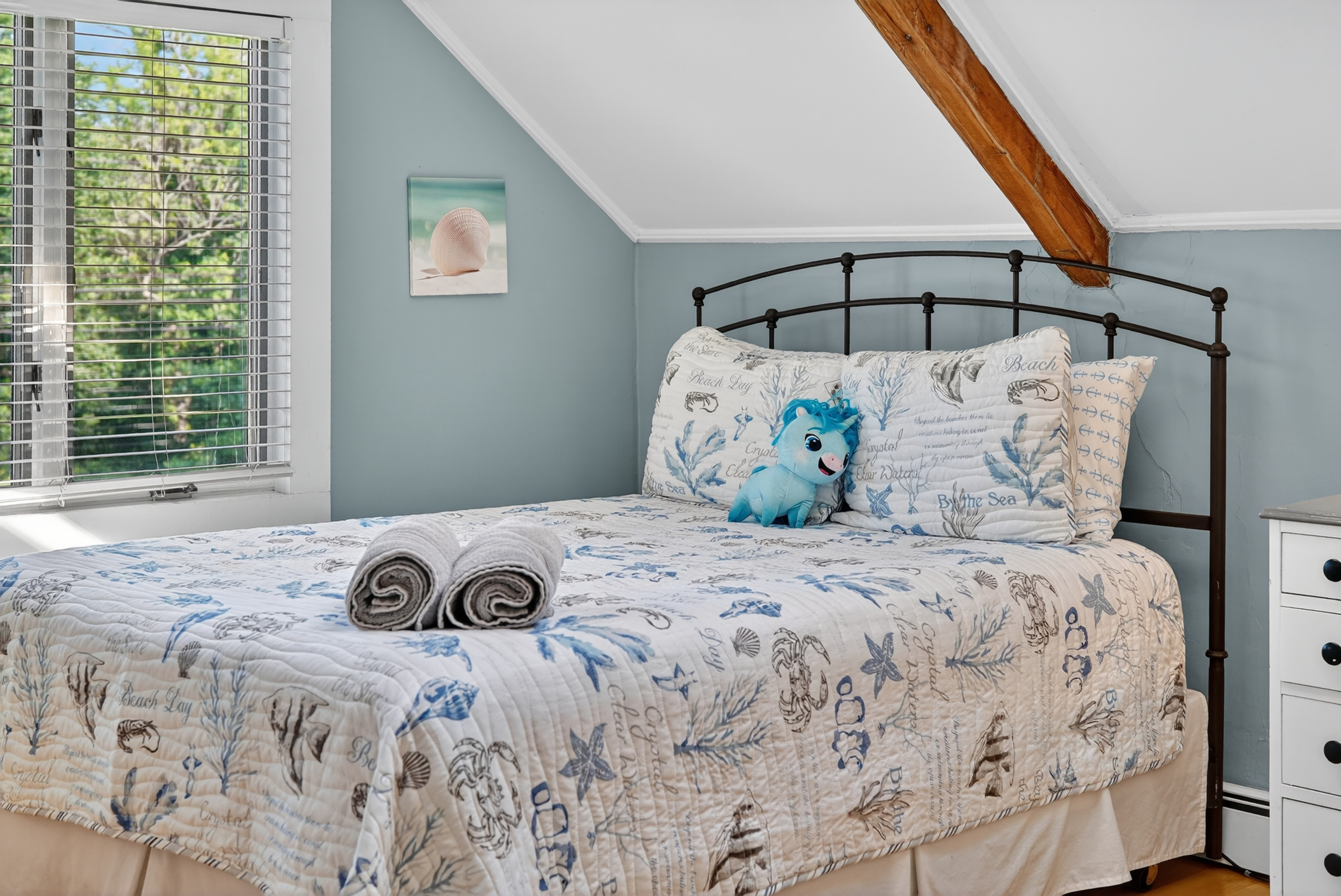 Cozy bedroom with soft coastal décor, comfortable bedding, and peaceful wooded views.