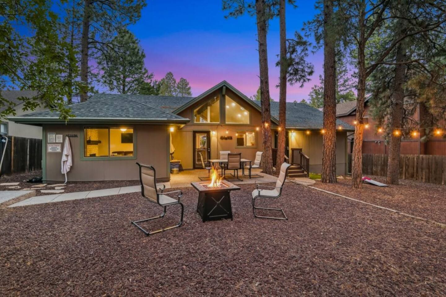 Outdoor gathering space with fire pit, lounge seating, and tall pine trees surrounding the yard.