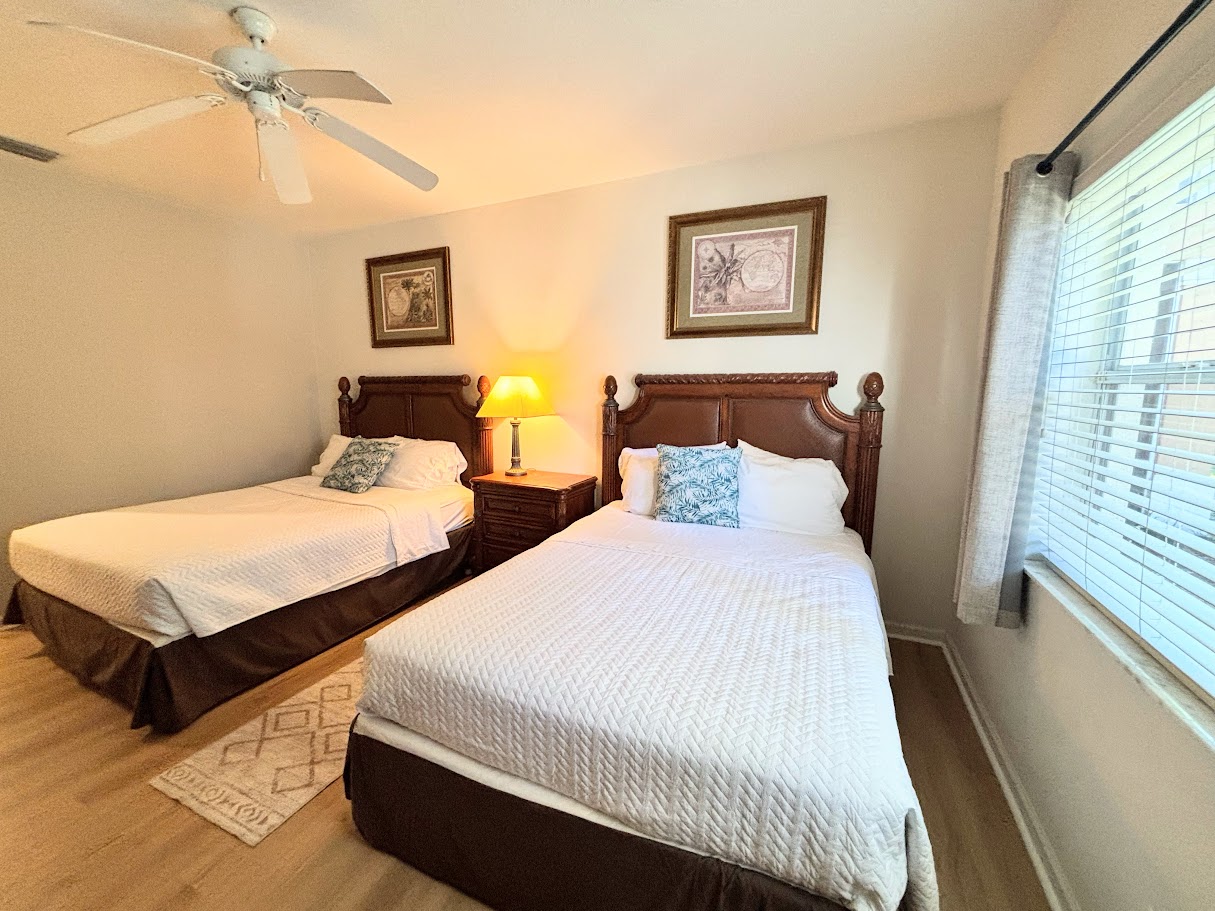 Bright bedroom with two comfortable beds, bedside lighting, and neutral decor.