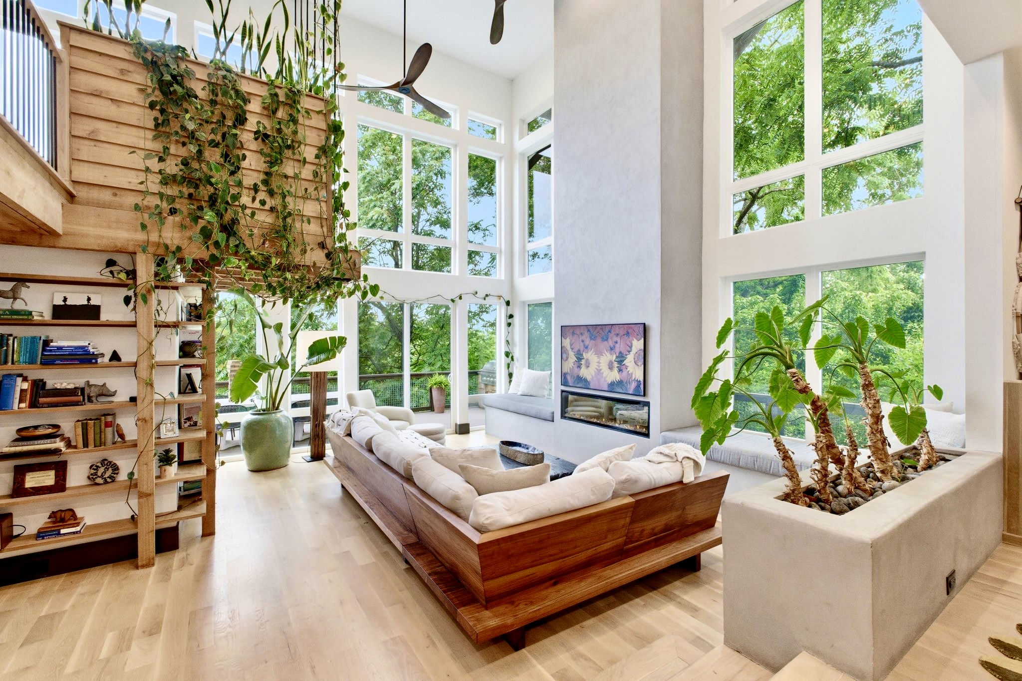 Light-drenched living area w/ lush greenery, spiral staircase & effortless indoor-outdoor flow.

