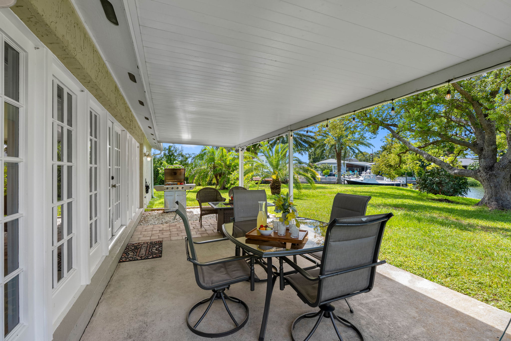 This patio blends indoor comfort with outdoor beauty, featuring a shaded roof, stylish furniture, and a scenic water view.