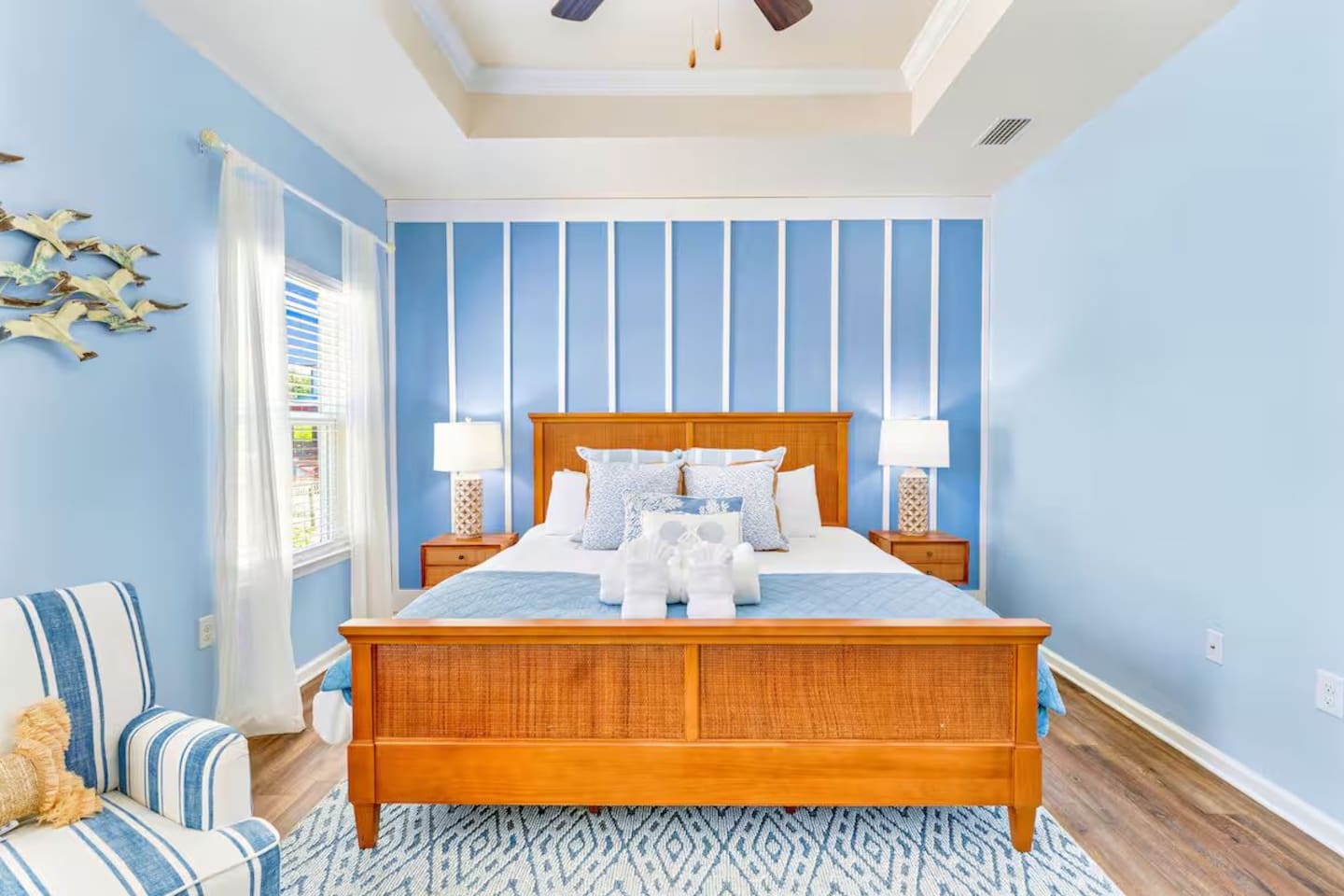 Primary Suite: Elegant King bedroom featuring an en suite bathroom, plush linens, ceiling fan, elegant bedside lamps, dresser, couch, and Smart TV.