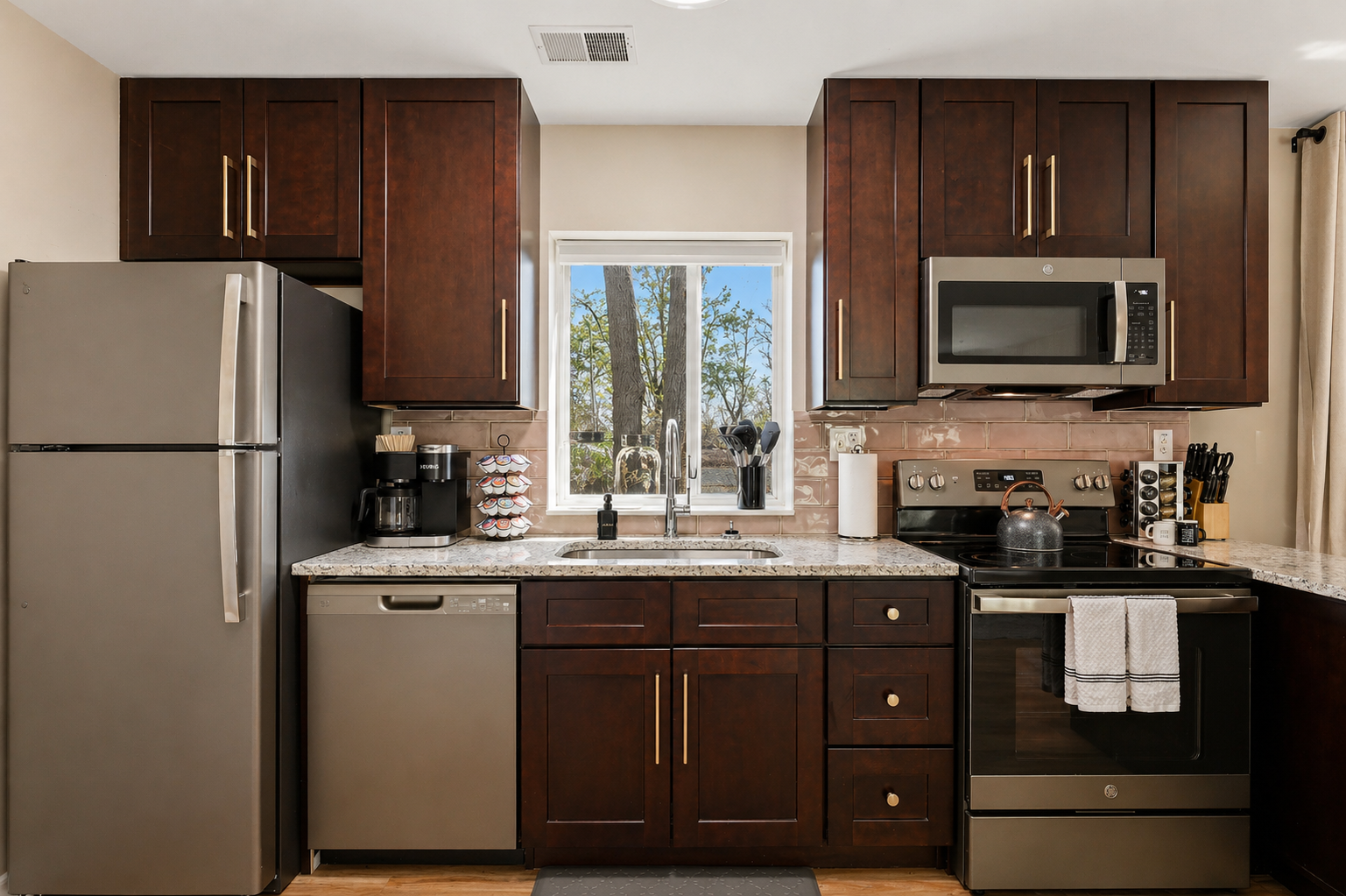 Welcome to a meticulously organized kitchen featuring elegant white cabinets and an array of essential appliances, including a stove, oven, microwave, and a sink. Enjoy the bright ambiance with a window that fills the space with natural light.