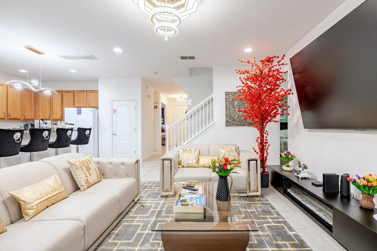 Main downstairs living room with a 98-inch TV and piano, open to the kitchen and dining area.
