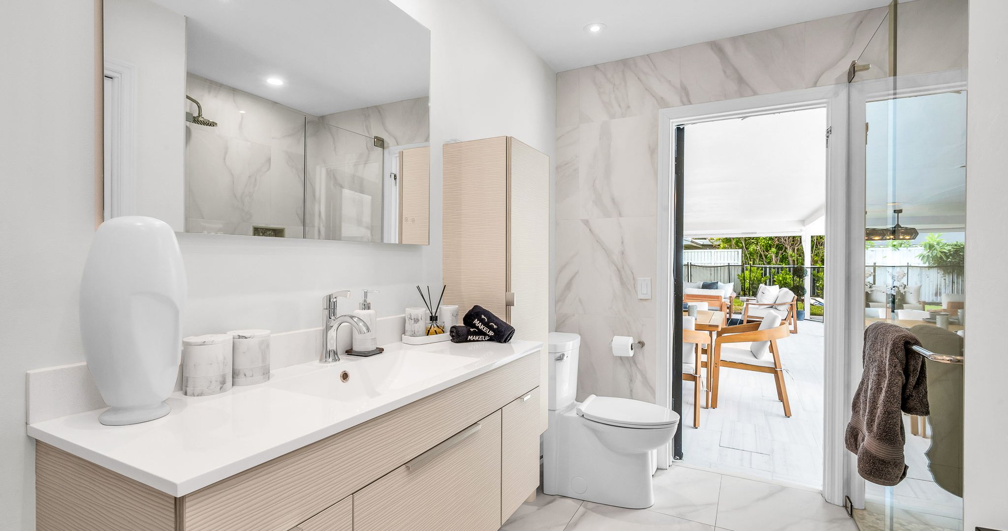 Elegant guest bathroom with sleek modern vanity, designer fixtures, and marble-inspired tile. Features a glass-enclosed shower and direct access to the outdoor lounge and pool area for seamless indoor-outdoor living