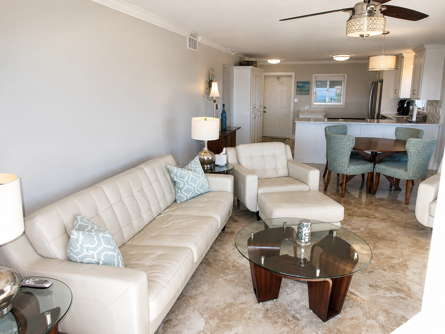 Modern living room with cream leather sofa, blue accents, and sleek open kitchen.