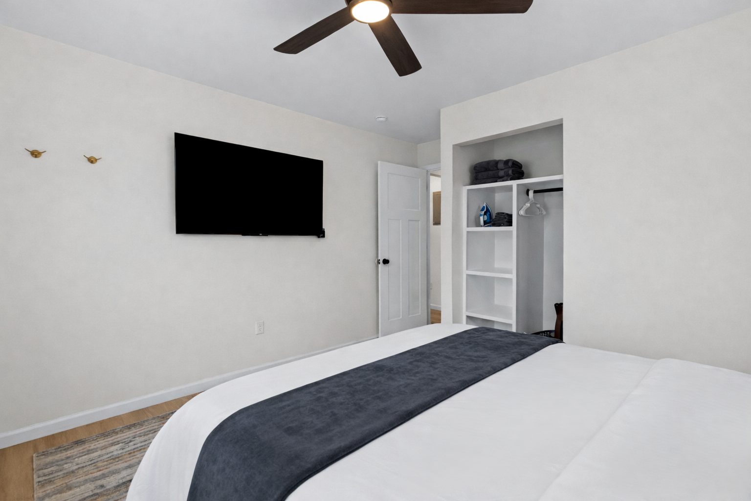 Relax in this well-appointed bedroom with a wall-mounted smart TV, ceiling fan, and open closet storage—designed for comfort and easy living.