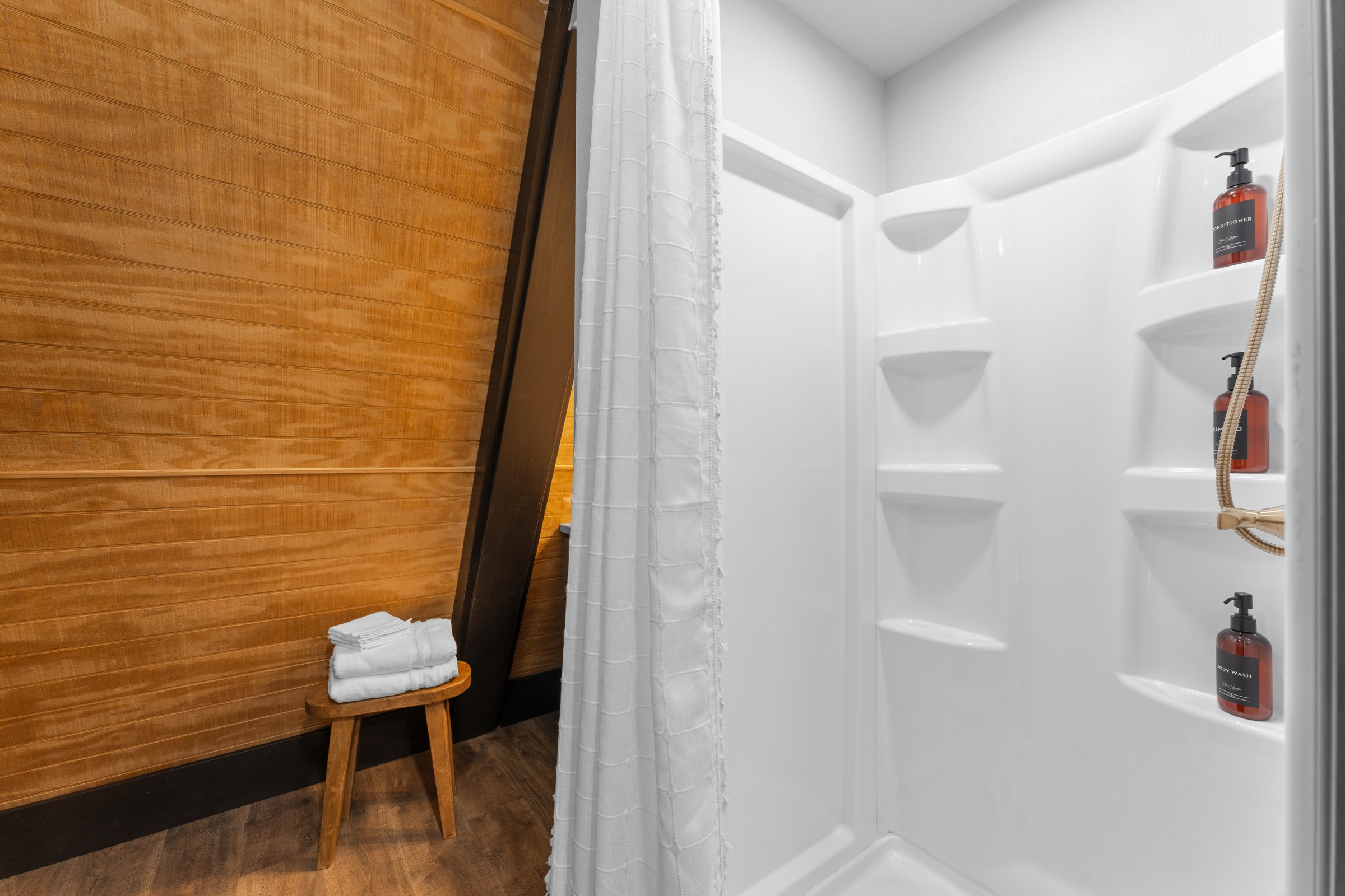 Step-in shower with toiletries and a wood towel stool. Fresh towels are stacked and ready for after the hot tub.