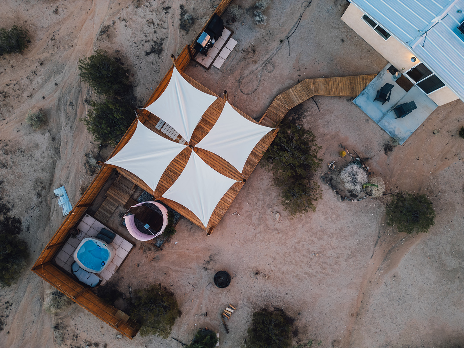 Aerial view of fenced backyard featuring private hot tub, outdoor shower, and lounge deck surrounded by desert landscape.