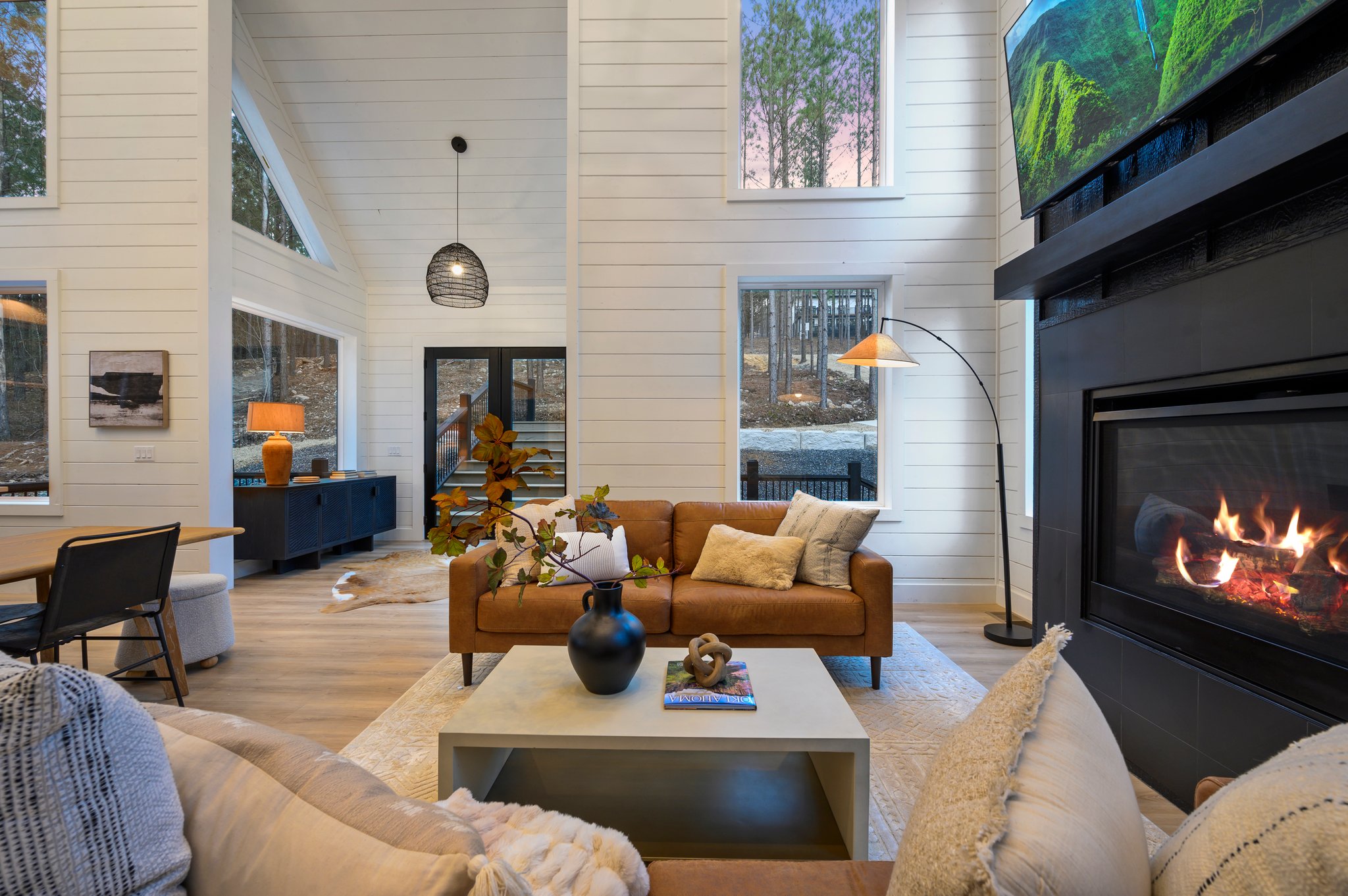 Soaring ceilings and dramatic windows create a bright, open living space surrounded by forest views.