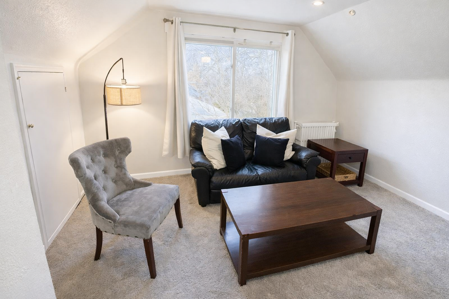 The living room is furnished with a cozy leather couch and accent chair, providing a comfortable seating arrangement. Additionally, there’s a supplementary AC unit to keep you cool during sweltering summer days.