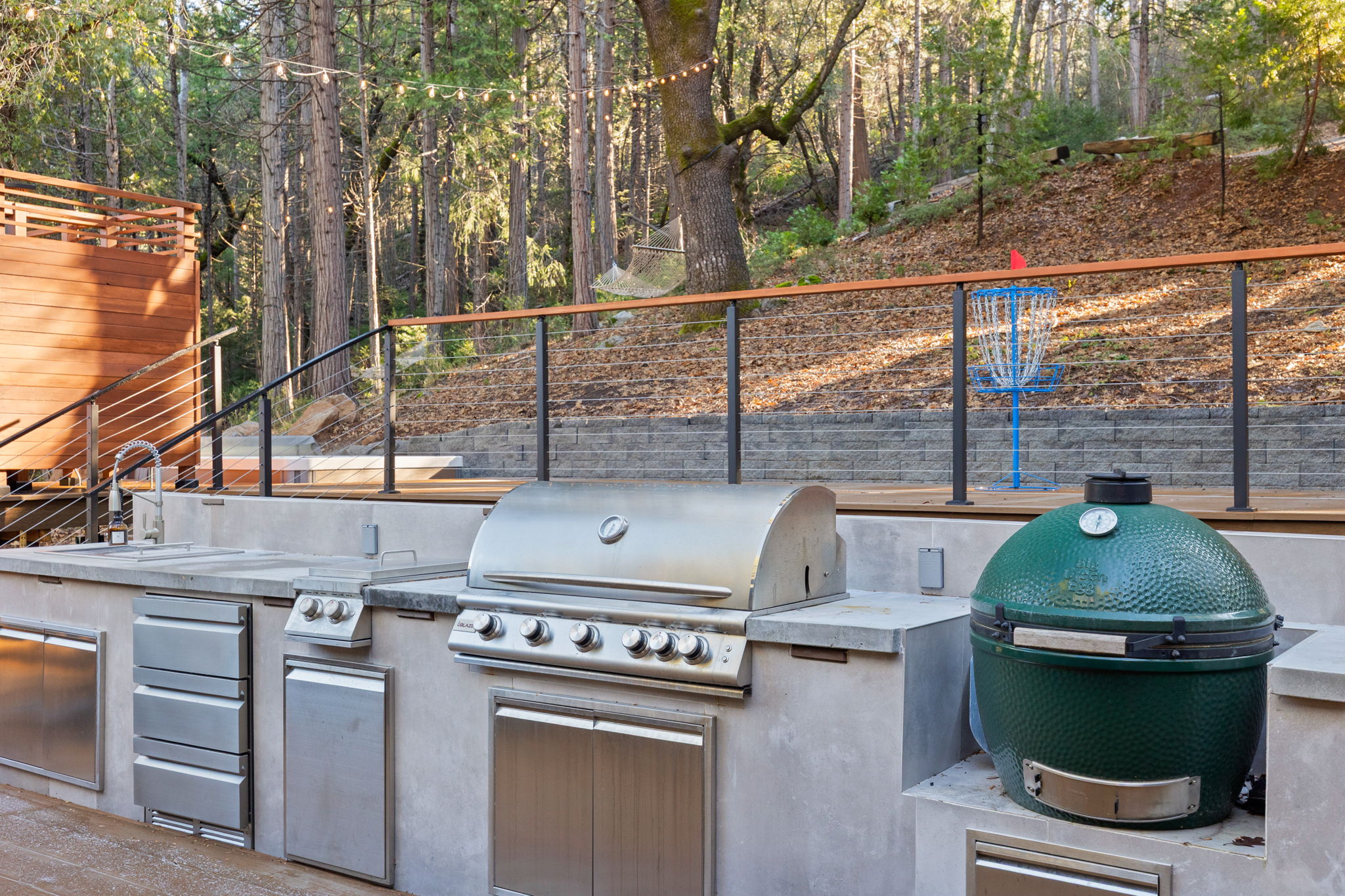 Outdoor kitchen complete with a smoker, gas grill, double burners, refrigerator drawers, sink and dual pull out garbage cans.