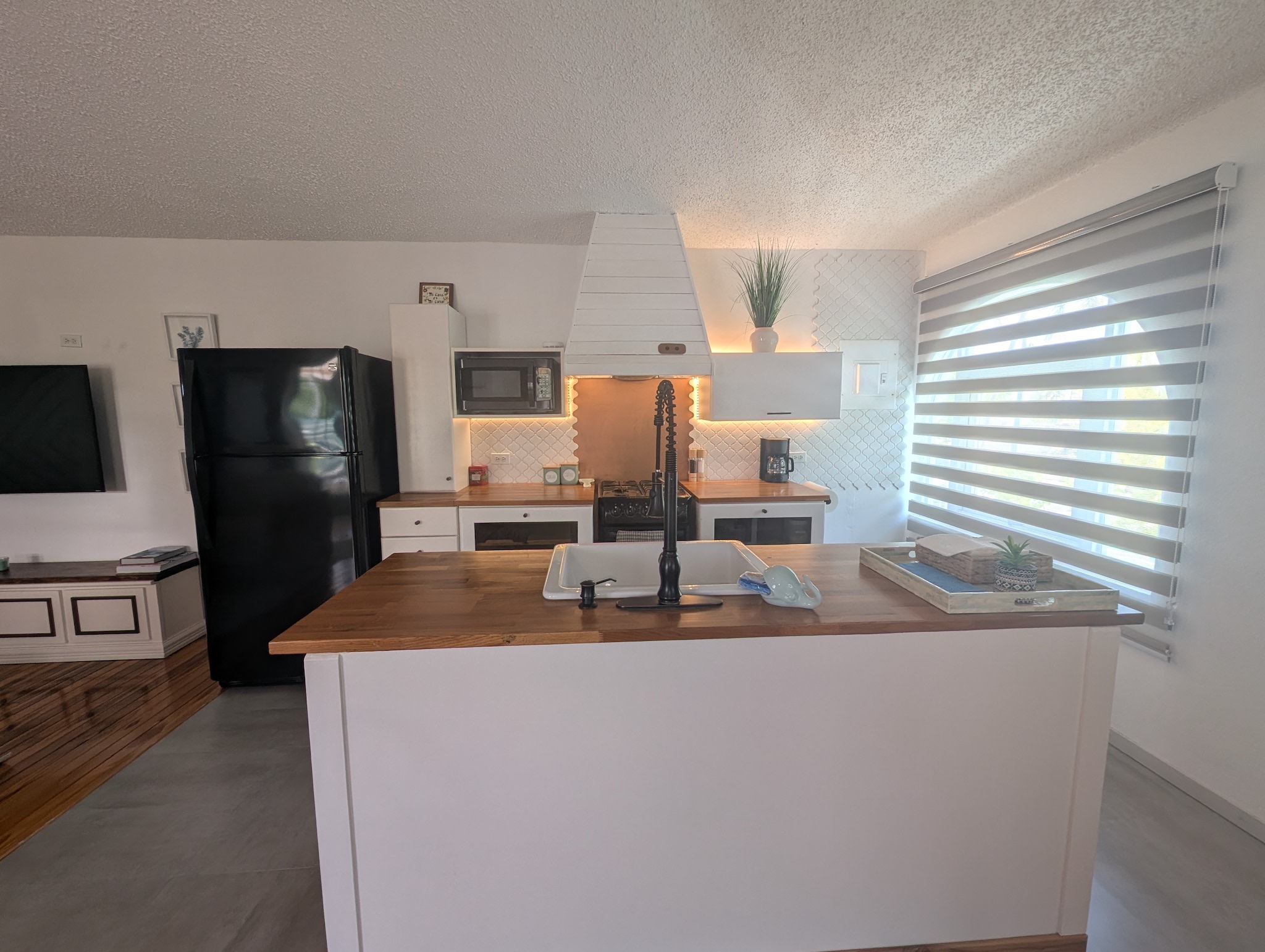 Fully equipped upstairs kitchen at Villa Coral featuring a white central island with a wood countertop, integrated sink, black refrigerator, modern white range hood, and warm ambient LED lighting in Dorado, Puerto Rico.
