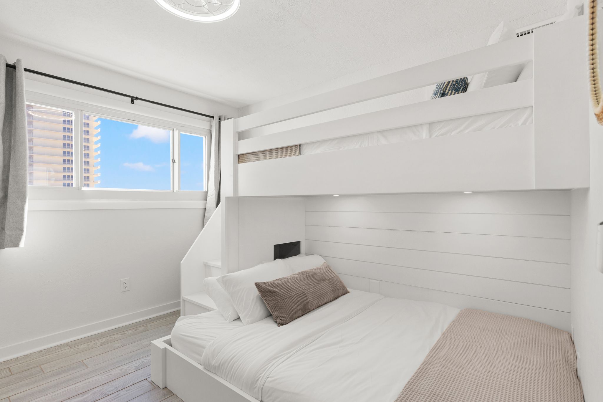 Guest bedroom featuring custom-built, adult-size bunks with a plush queen bed on the bottom and a Twin XL on top—a high-end, space-smart setup with built-in charging cubbies feels more like a boutique stay than a typical bunk room. 