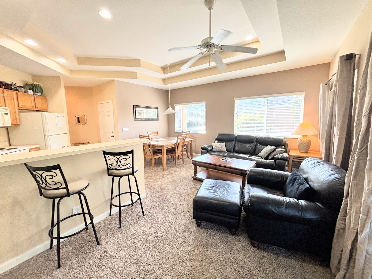 Updated living area with comfortable leather seating, open-concept layout, breakfast bar, dining space, and plenty of natural light.