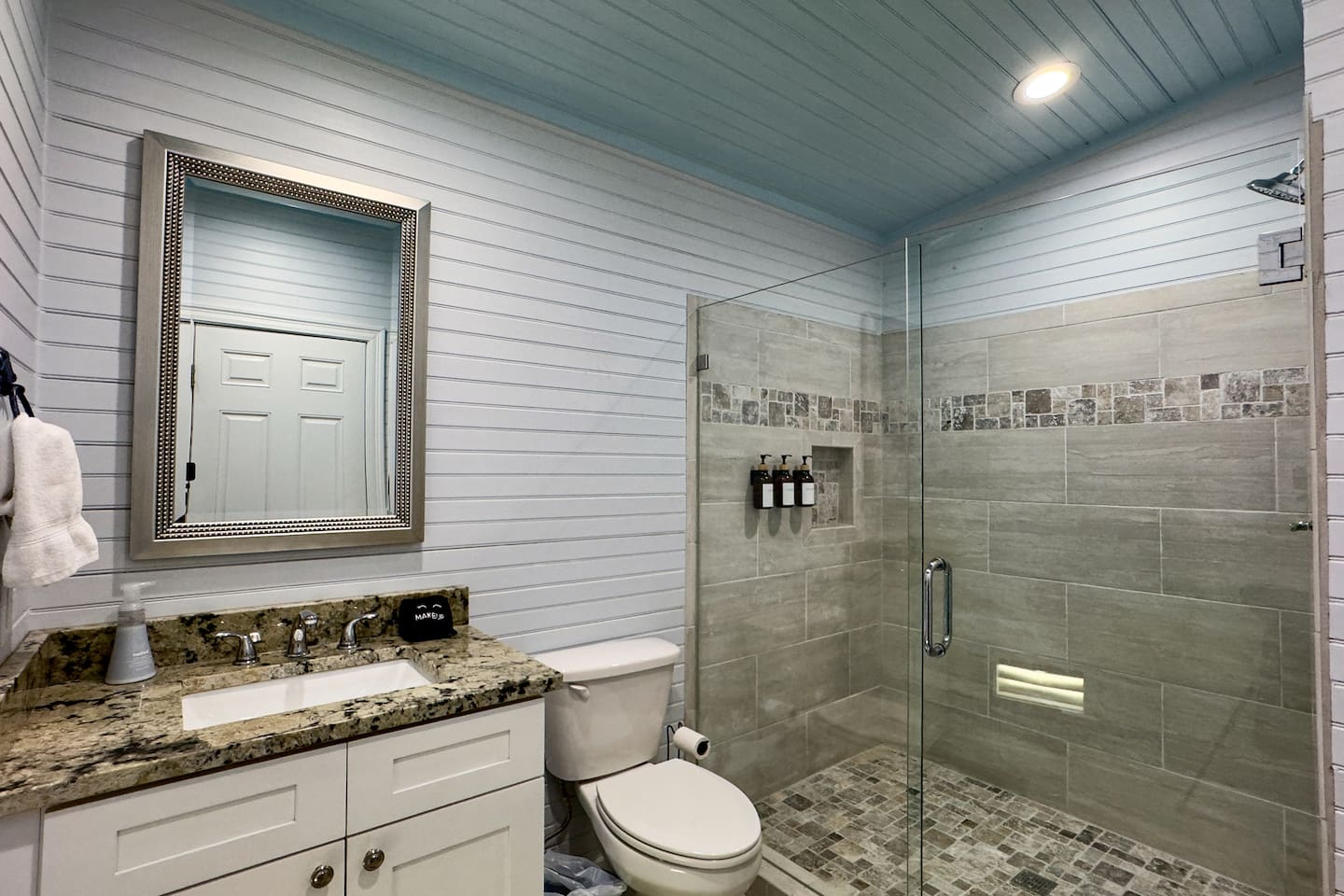 Stylish bathroom with a glass walk-in shower, granite vanity, and bright coastal design.