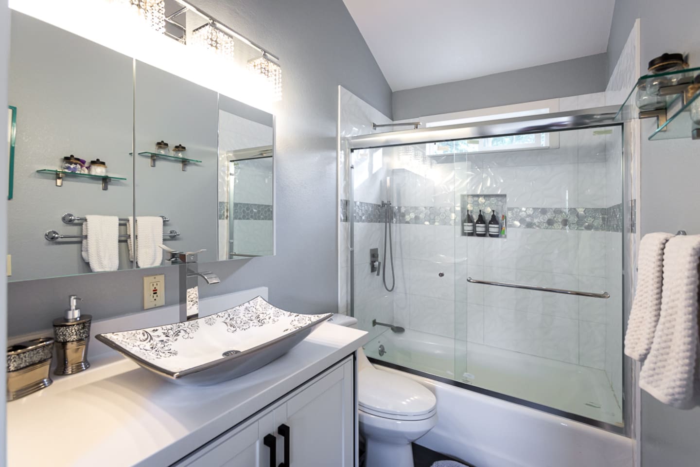 - Modern bath with glass enclosed shower, rainfall head, and decorative tile accents
- Elegant vessel sink and chrome fixtures complement the bright, airy design
- Plush towels and wall mounted amenities offer a touch of hotel style comfort