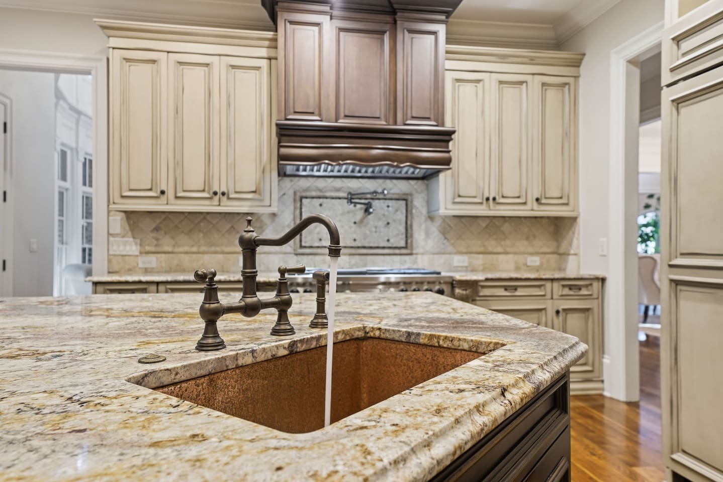 This open kitchen features beautiful cream wood cabinetry, sleek granite countertops, and an island that comfortably seats four. The bright, airy design makes it the perfect place to cook, gather, and share meals together.